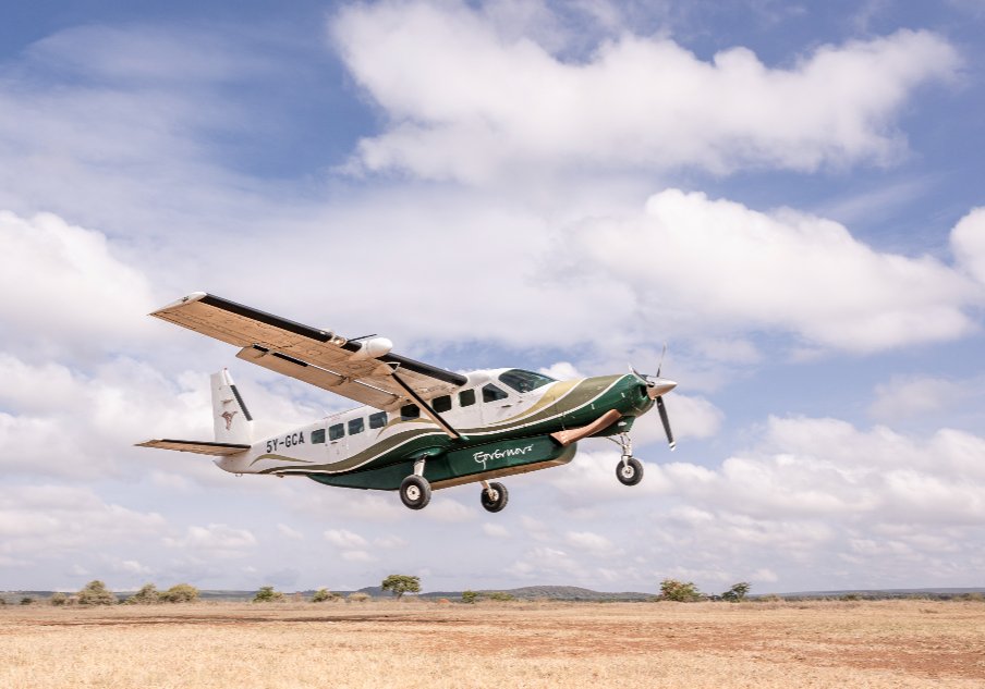 A Cessna Caravan 208 lifting off over open savanna under a cloudy blue sky
